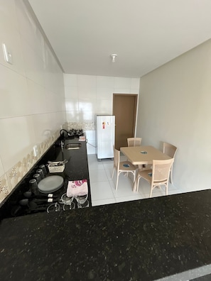 A compact kitchen with a black countertop, white tiled backsplash, a white refrigerator, and a dining area with a table and chairs.