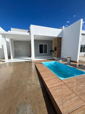 A modern house with a swimming pool, a covered patio, and a brick wall.