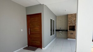 A spacious hallway with a wooden door, a glass door, and a brick fireplace. - Casa Corais Beach Francês (Marechal Deodoro)