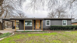 Ein modernes, einstöckiges Haus mit dunkler Fassade, einer Holztür und einem überdachten Eingangsbereich.