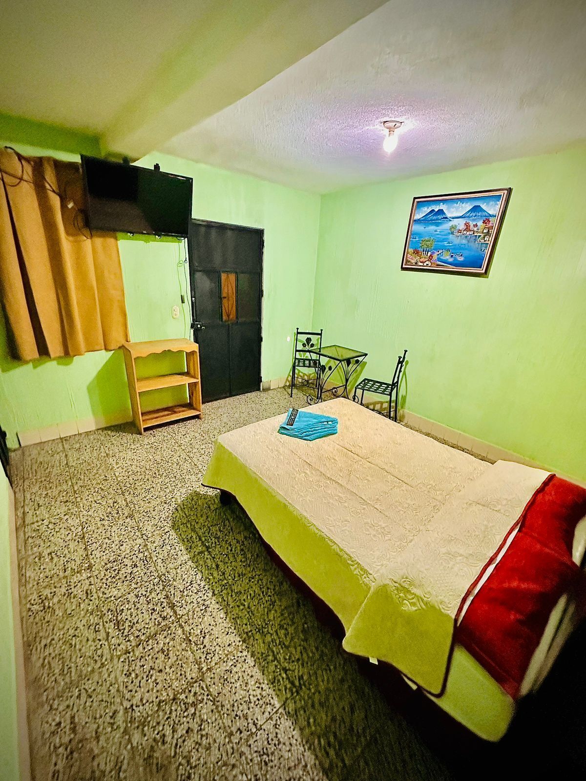 Una habitación con una cama, un escritorio, una silla, un televisor en la pared y un cuadro.