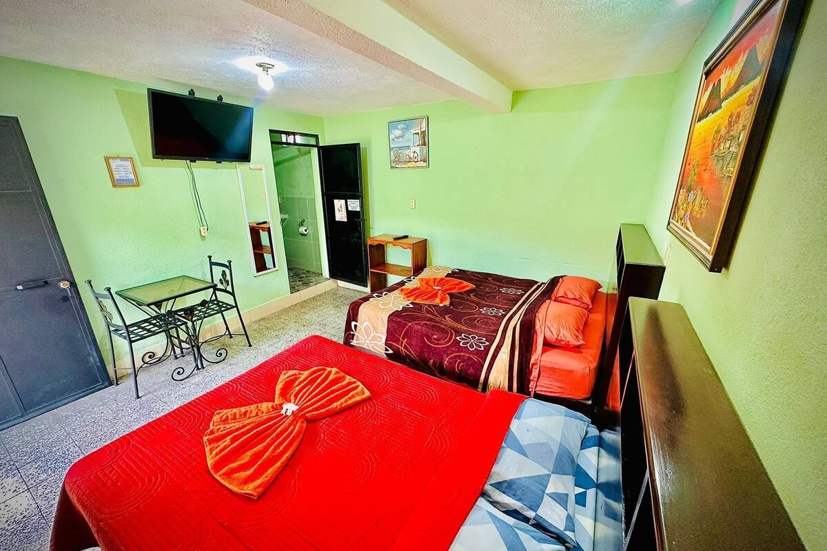 A hotel room with a bed, a desk, a chair, a TV, and a door.