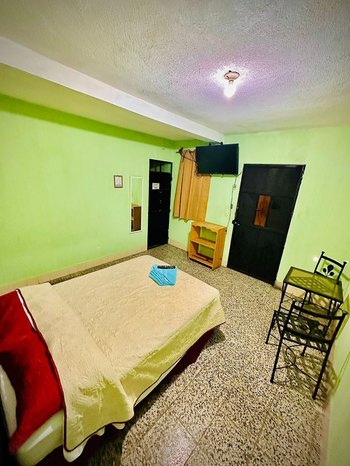 A room with a bed, a desk, a chair, a television mounted on the wall, and a door.