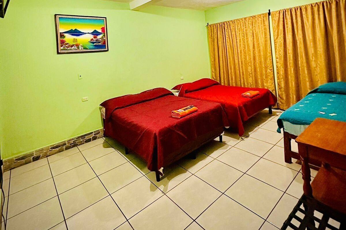 A room with three beds, a painting on the wall, and a window with curtains.