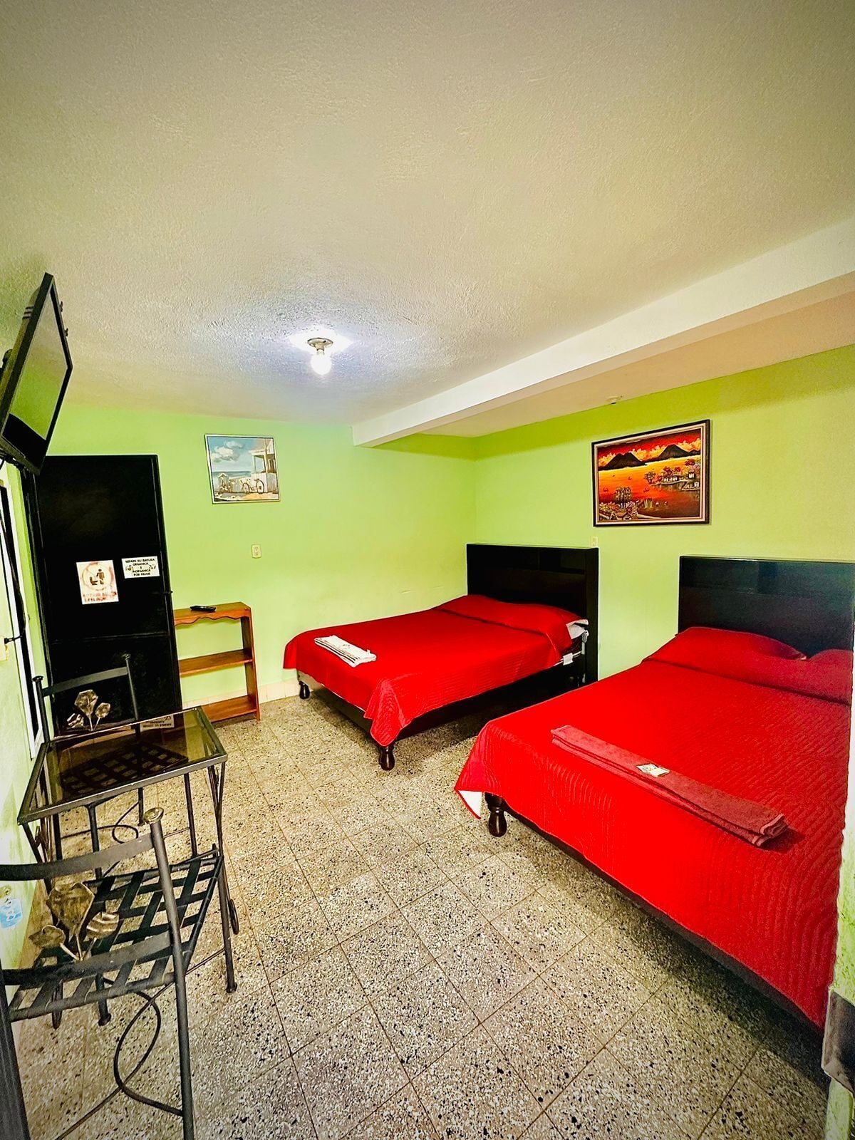 A room with two single beds, a small desk with a chair, a television, and a painting on the wall.