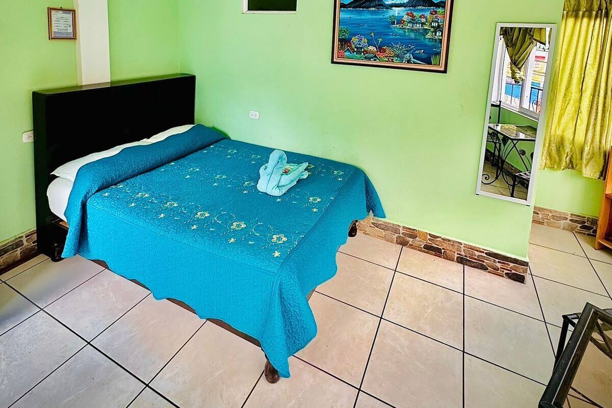 A room with a bed, a ceiling fan, a framed picture, and a window with curtains.