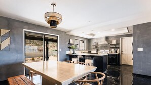 A modern kitchen with a large island, dark countertops, and a dining area with a wooden table and chairs. - @ Marbella Lane - Zen-like Ambiance 3BR Home in JT (Joshua Tree)