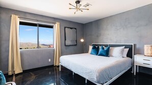 A modern bedroom with a large bed, a bedside table, a floor lamp, and a view of the outdoors. - @ Marbella Lane - Zen-like Ambiance 3BR Home in JT (Joshua Tree)