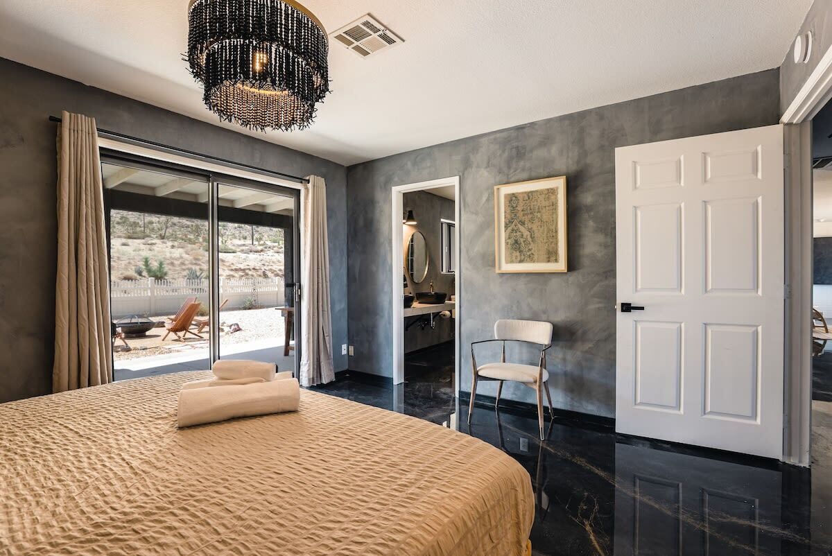 A bedroom with a large bed, a chair, a door, and a view of the outside.