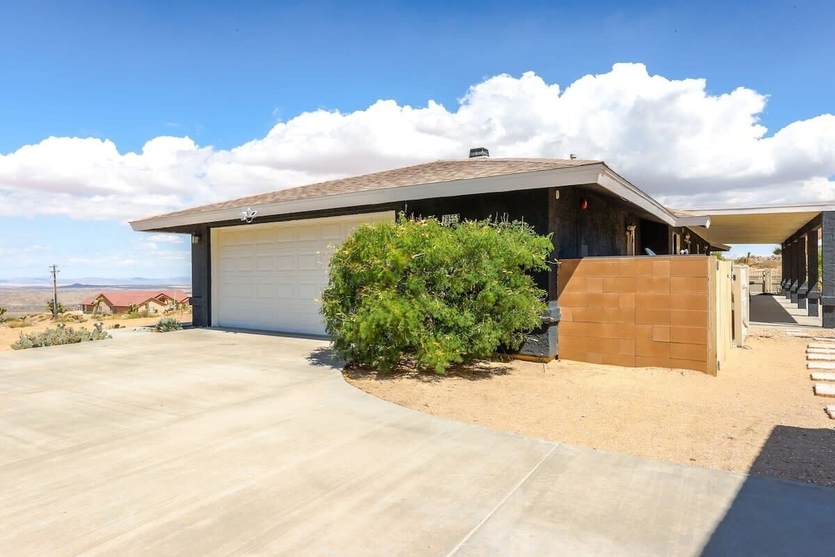 A modern single-story house with a garage, a small bush, and a clear view of the desert landscape.