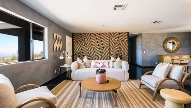 A modern living room with a sofa, coffee table, and chairs, a patterned wall, and a view through large windows. - @ Marbella Lane - Zen-like Ambiance 3BR Home in JT (Joshua Tree)