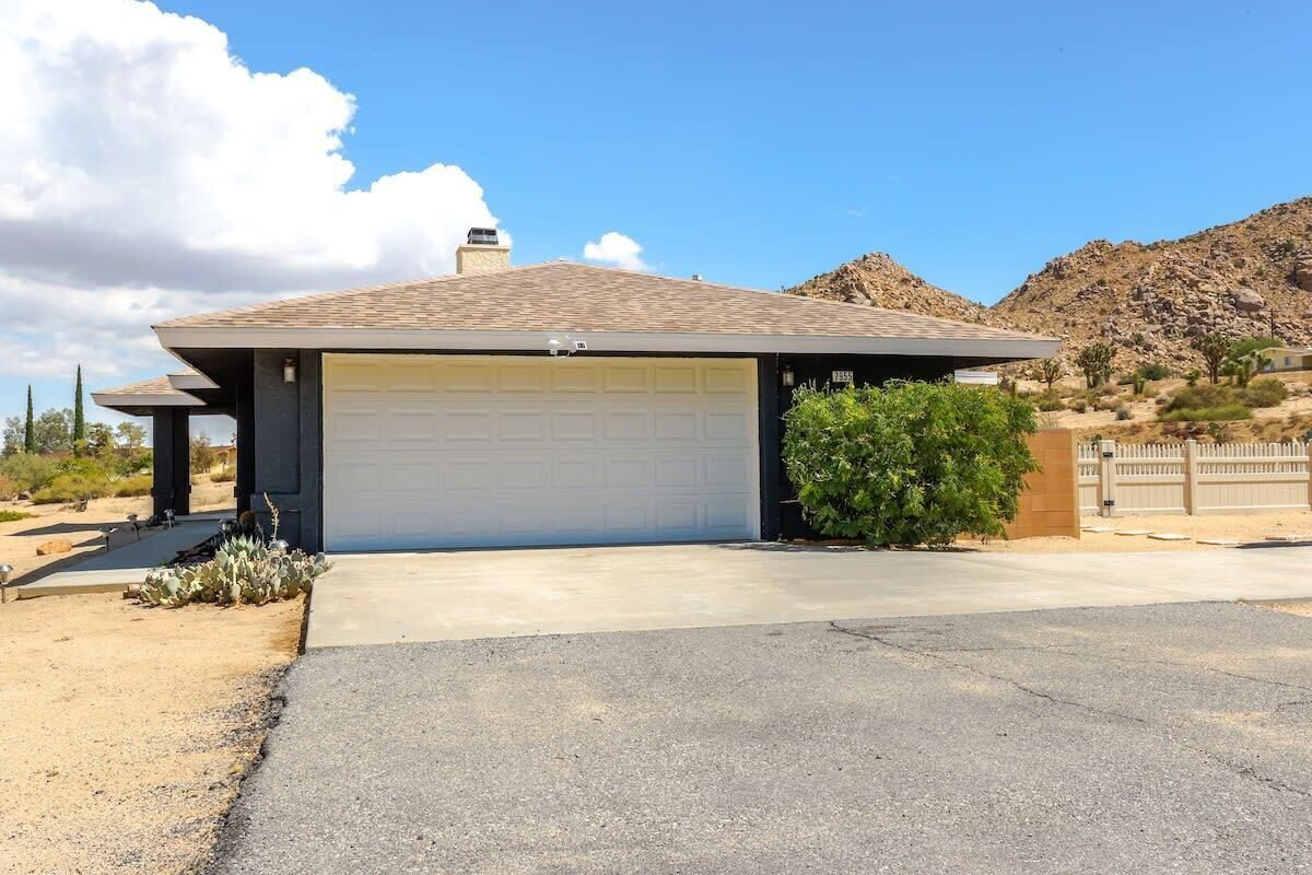 A single-story house with a garage, surrounded by desert vegetation and a mountain in the background.