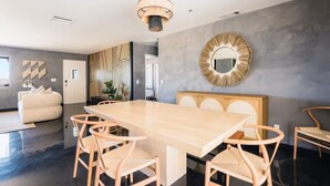 A modern dining area with a long wooden table, six wicker chairs, a round mirror, and a geometric wall design. - @ Marbella Lane - Zen-like Ambiance 3BR Home in JT (Joshua Tree)
