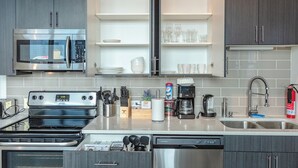 A modern kitchen with stainless steel appliances, open shelving, and a dishwasher. - Luxury Studio Apartment Near McCormick Place & Soldier Field (Chicago)