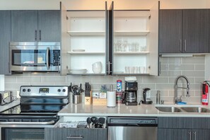 A modern kitchen with stainless steel appliances, open shelving, and a dishwasher. - Luxury Studio Apartment Near McCormick Place & Soldier Field (Chicago)