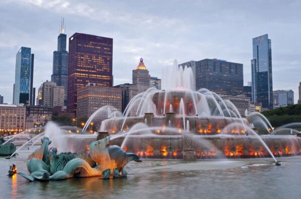 A cityscape with a prominent fountain and modern buildings in the background.