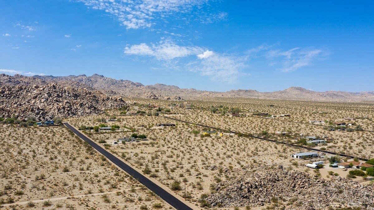 A desert landscape with sparse vegetation, a paved road, and scattered buildings.