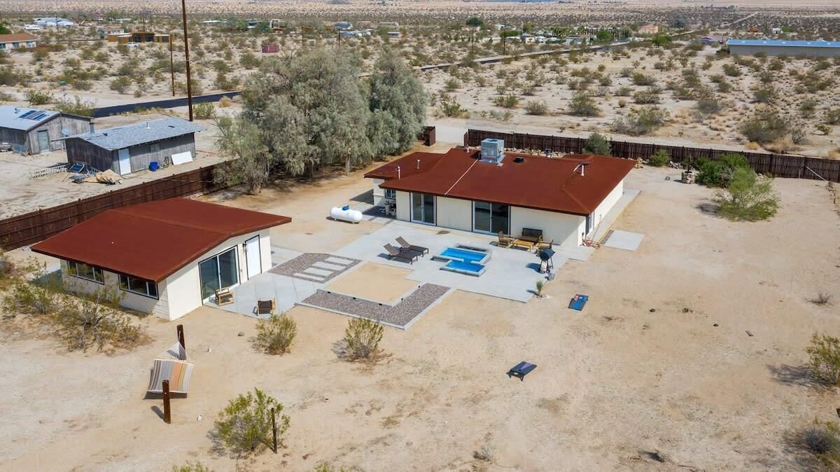 A modern house with a large patio, a swimming pool, and a fenced yard in a desert environment.