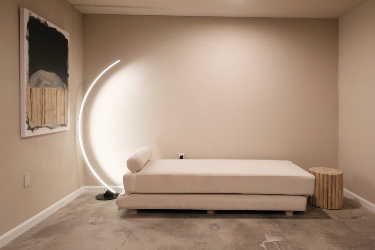 Et minimalistisk rum med en hvid sofa, et rundt bord og en vægmonteret lampe.