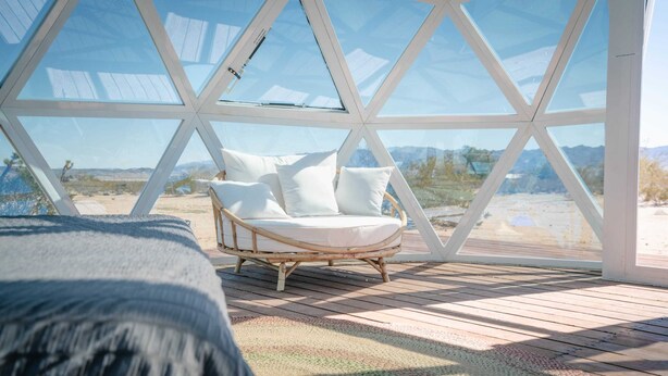 Une pièce chaleureuse avec une grande fenêtre en forme de dôme de verre, un fauteuil en osier agrémenté de coussins et un plancher en bois.
