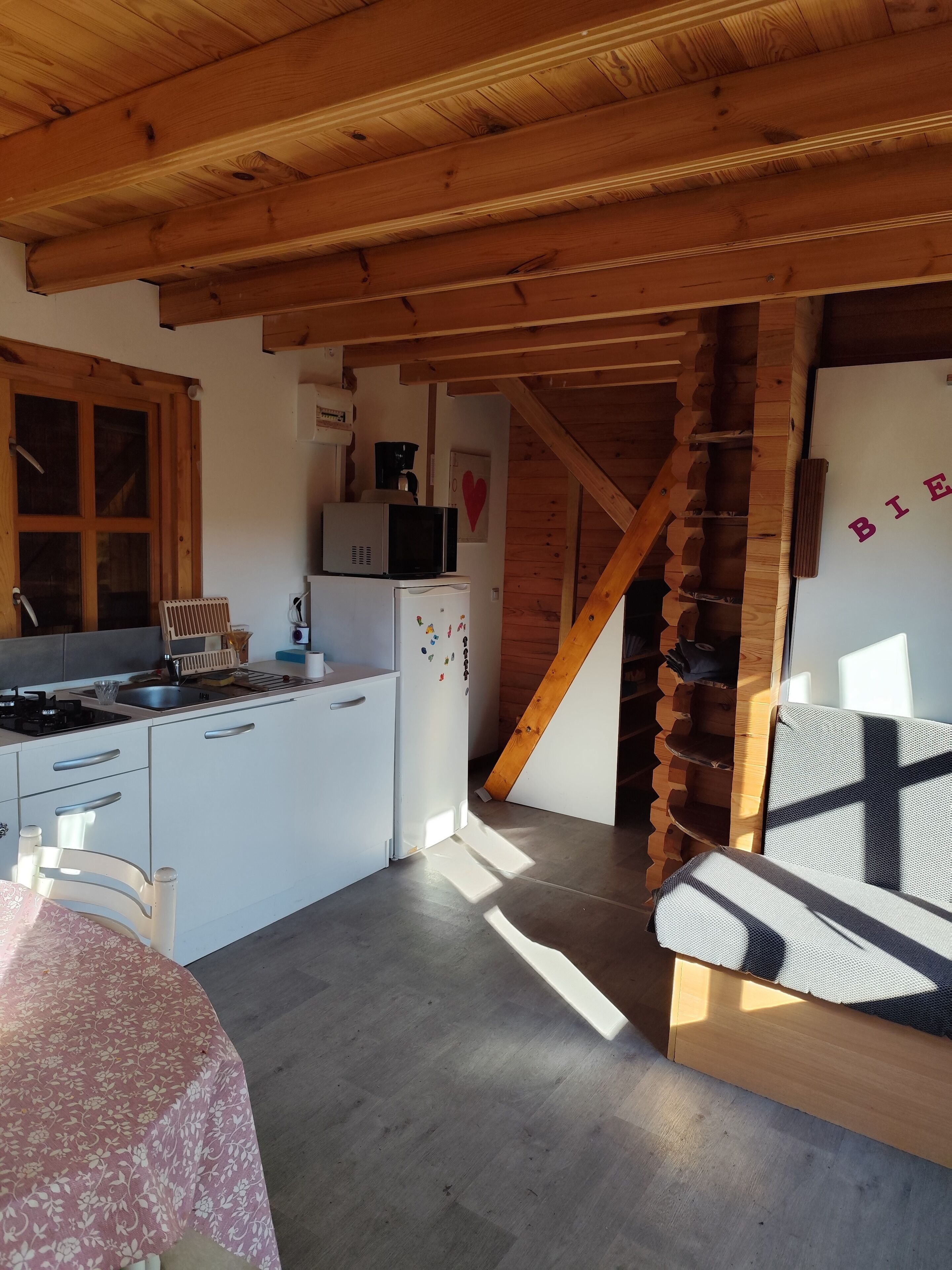 Cocina compacta con armarios blancos, un refrigerador y un microondas. Una escalera de madera conduce a otro nivel.