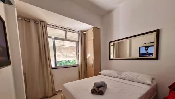 A hotel room with a bed, a window with curtains, a mirror, and a television. - 360 Leme Beach Anchieta By SUHCasa (Rio de Janeiro)