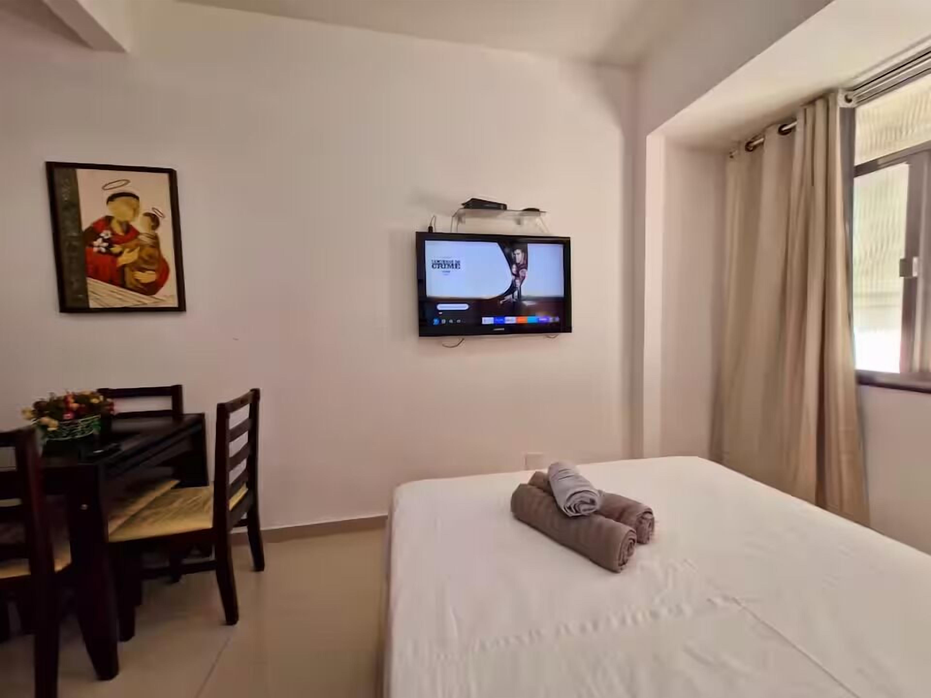 Ein Hotelzimmer mit Bett, Schreibtisch mit Stuhl, Wandfernseher und einem Vorhangfenster.