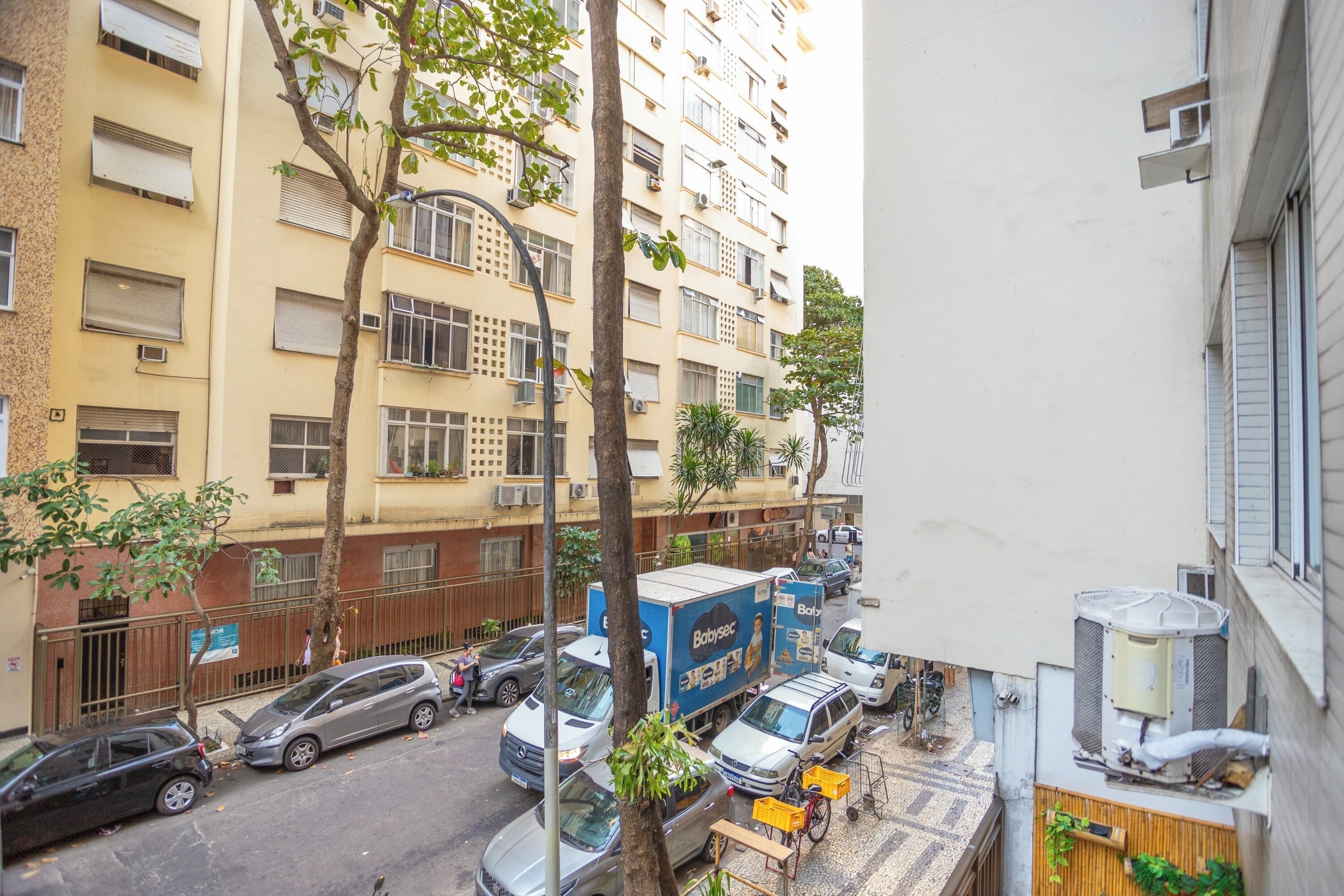 Un edificio residencial de varios pisos, con automóviles estacionados y un camión de reparto en la calle.