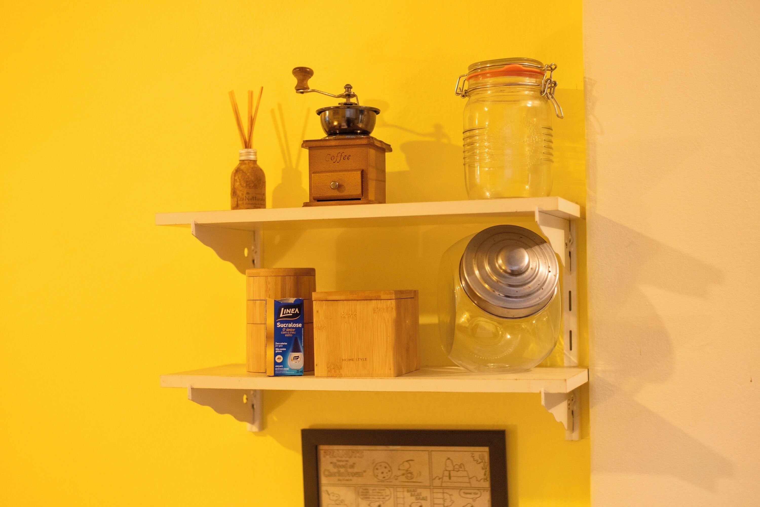 A shelf with a coffee grinder, a jar, a box of sucralose, and a framed drawing.