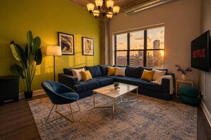 A living room with a sectional sofa, a coffee table, a floor lamp, and a large window with a city view.