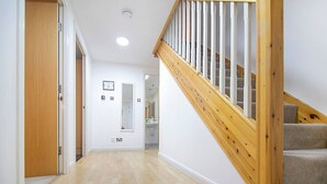 Un couloir avec un escalier en bois, un miroir et une porte donnant sur une salle de bain.