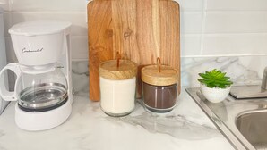 A kitchen with a white coffee maker, a wooden cutting board, two glass jars with lids, and a small potted plant. - 4 people, 2 Full beds (bunk beds), AC, 1 bedroom, bathroom and kitchen. (San Juan)