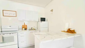 A modern kitchen with white cabinetry, a built-in oven, a microwave, and a small island with stools. - 4 people, 2 Full beds (bunk beds), AC, 1 bedroom, bathroom and kitchen. (San Juan)