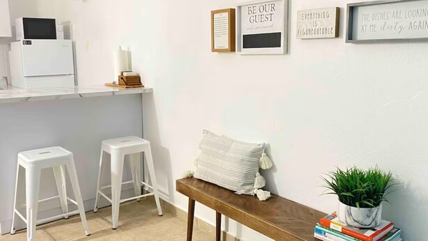 A kitchen with white stools, a bench with books and a plant, and motivational wall art. - 4 people, 2 Full beds (bunk beds), AC, 1 bedroom, bathroom and kitchen. (San Juan)
