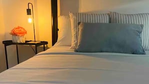 A neatly made bed with a striped pillow and a vase of flowers on a bedside table. - 4 people, 2 Full beds (bunk beds), AC, 1 bedroom, bathroom and kitchen. (San Juan)