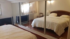 A hotel room with a large mirror reflecting the bed and a chair, a wooden headboard, a bedside table with a lamp, and a window with curtains. - Rental Villa, 200m², 6 bedrooms, sleeps up to 12, swimming pool, Montauroux (Montauroux)