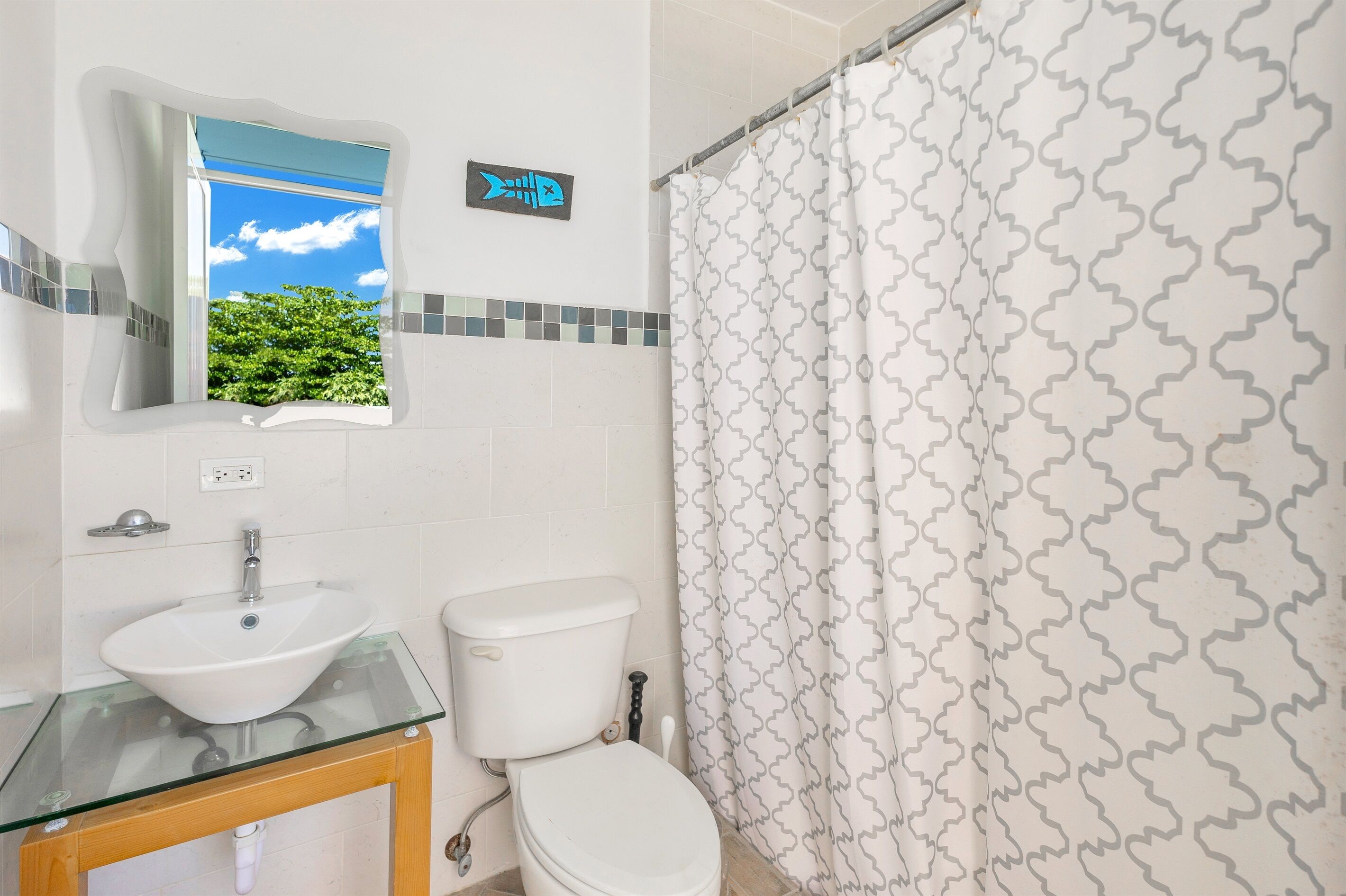 A bathroom with a glass sink, white toilet, and patterned shower curtain.