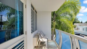 A balcony with a view of palm trees, a white wall, and a window with blinds. - Steps to Beach/Pool & Jacuzzi/Wave Coast Suite 8! (Rincon)