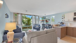 A modern living room with a grey sofa, a round glass coffee table, and a TV on a wall. - Steps to Beach/Pool & Jacuzzi/Wave Coast Suite 8! (Rincon)