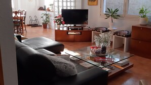 Una sala de estar con un sofá, una mesa de centro de vidrio, un televisor y un comedor con una mesa y sillas.