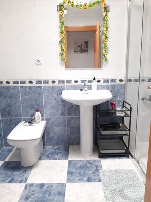 Bany amb un lavabo pedestal blanc, un vàter i una dutxa amb envà.
