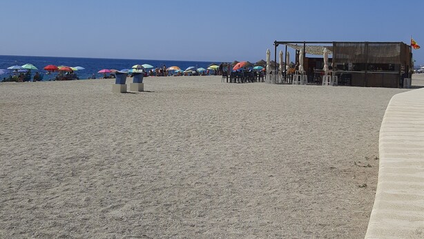 Una playa con sombrillas y sillas, un área de bar y una vista despejada del océano.