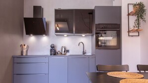 Une cuisine moderne avec des meubles de couleur grise, un four encastré et un coin repas comprenant une table et des chaises.