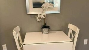 A white dining table with two chairs, a framed mirror above it, and a small potted plant on the table. - ♥ of SSI Bungalow, Quick walk to beach and food ☼ (St. Simons Island)