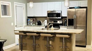 A modern kitchen with white cabinets, stainless steel appliances, and a central island with bar stools. - ♥ of SSI Bungalow, Quick walk to beach and food ☼ (St. Simons Island)