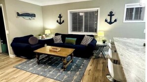 A living room with a dark blue sofa, a wooden coffee table, and a window with blinds. - ♥ of SSI Bungalow, Quick walk to beach and food ☼ (St. Simons Island)
