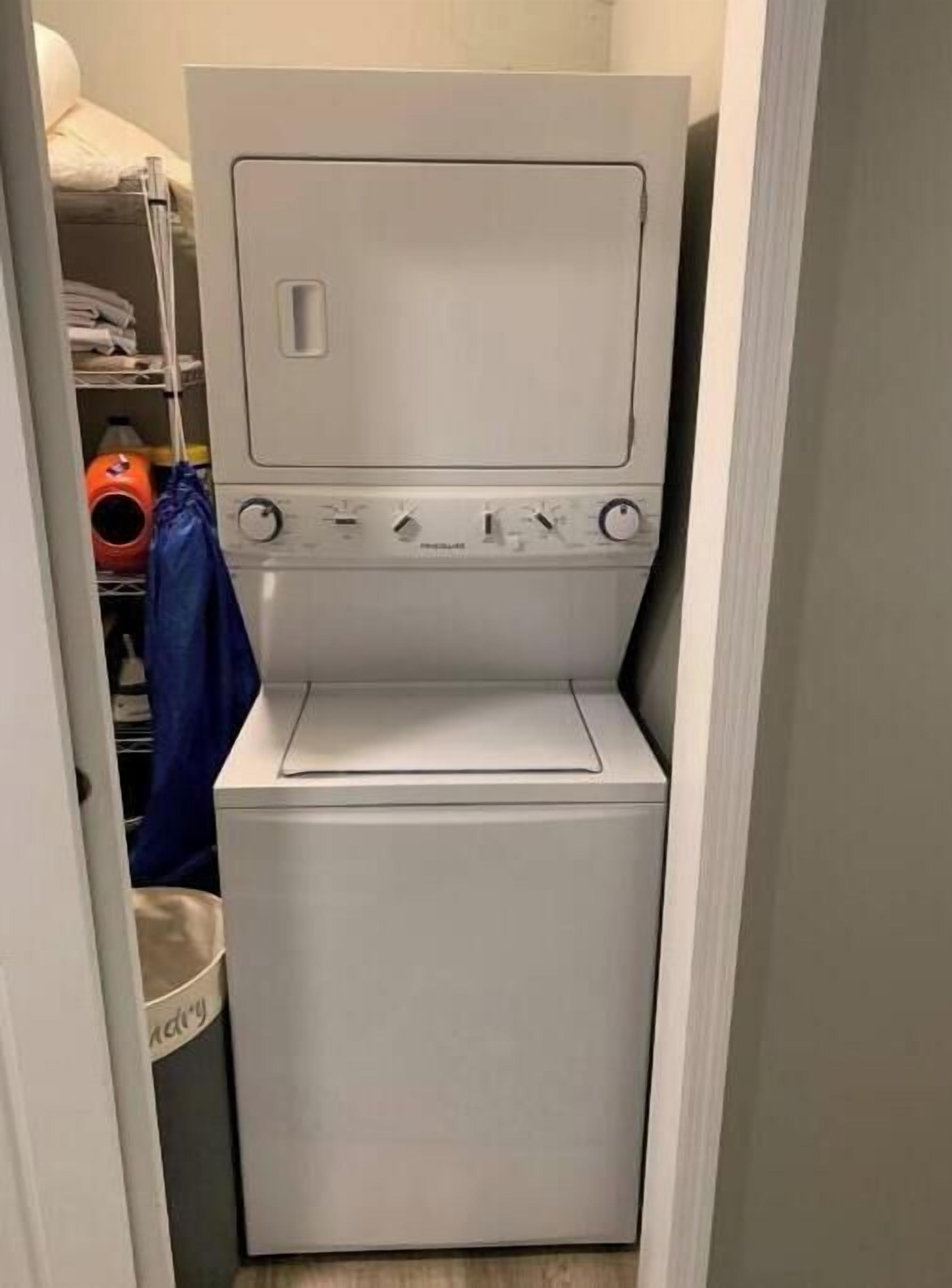 Una lavadora y secadora de carga frontal, de color blanco y tamaño compacto, en un cuarto de lavado con un estante pequeño en la parte superior.