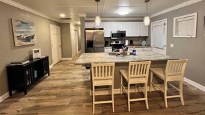 A kitchen with a central island, wooden chairs, and a black cabinet. - ♥ of SSI Bungalow 2, Quick walk to beach and food ☼ (St. Simons Island)