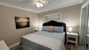 A bedroom with a bed, nightstands, a ceiling fan, a window with blinds, and a painting on the wall. - ♥ of SSI Bungalow 2, Quick walk to beach and food ☼ (St. Simons Island)