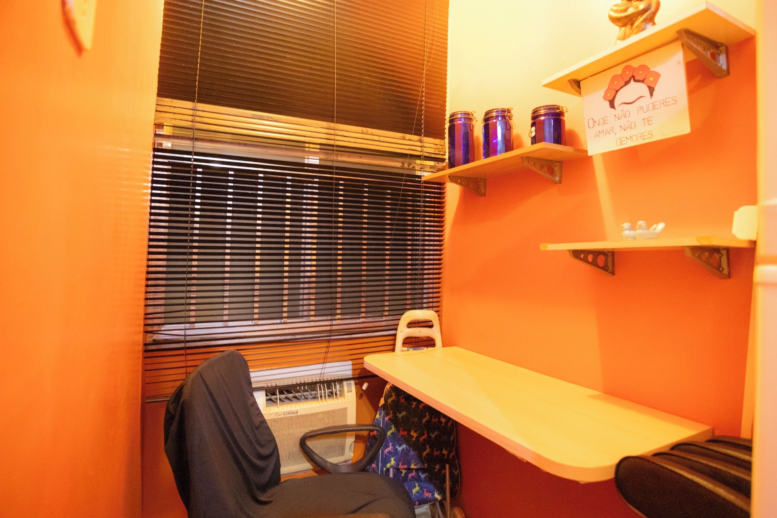 A small room with a window, a chair, a desk, and shelves with items.